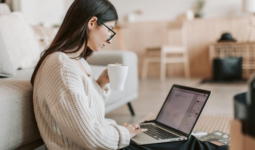 Woman working remotely on a laptop with a cup in hand