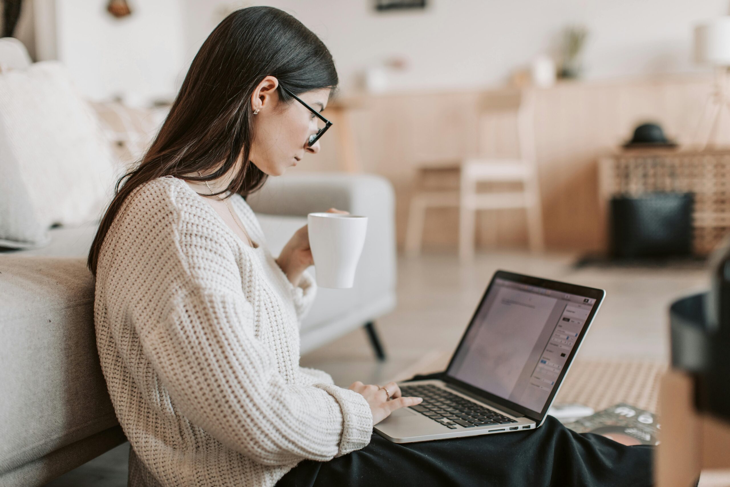 Woman working remotely on a laptop with a cup in hand